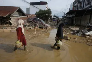 Hingga Kamis (5/12/2025) malam, listrik belum menyala, sehingga jalanan masih gelap gulita. Tampak dalam foto, para penyintas berjalan melewati reruntuhan mobil di area terdampak banjir bandang di Aceh Tamiang, Sumatera, Indonesia, Kamis 4 Desember 2025. (AP Photo/Binsar Bakkara)