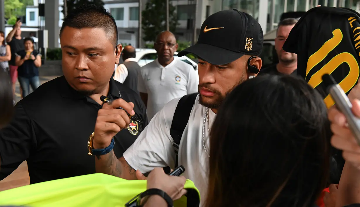 Penyerang Brasil, Neymar (tengah) menandatangani jersey penggemar saat tiba sebuah hotel di Singapura (7/10/2019).  Brasil akan menghadapi Senegal pada pertandingan persahabatan di Singapore National Stadium pada 10 Oktober 2019. (AFP Photo/Roslan Rahman)