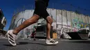Sebagai informasi, edisi tahun ini, Maraton Internasional Palestina, diikuti oleh lebih dari 13.000 pelari, termasuk sekitar 1.000 peserta internasional dari 75 negara. Tampak dalam foto, para pelari melewati tembok pemisah Israel saat mereka berkompetisi dalam Maraton Palestina di kota Betlehem, Tepi Barat, Jumat 8 Mei 2026. (AP Photo/Mahmoud Illean)