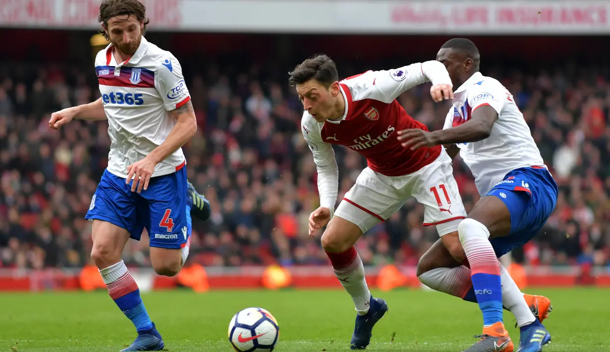 Gelandang Arsenal, Mesut Ozil, ditarik oleh bek Stoke Bruno Martins Indi, pada laga Premier league di Stadion Emirates, London, Minggu (1/4/2018). Arsenal menang 3-0 atas Stoke. (AFP/Oliver Greenwood)