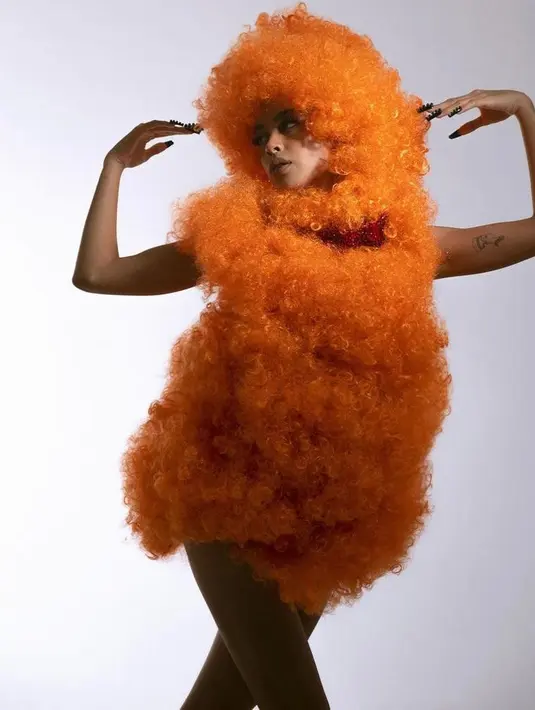 Dalam outfit selanjutnya, Eva juga sukses mencuri perhatian dengan outfit berbulu dengan warna orange mencolok yang begitu pop-out di atas backdrop berwarna putih polos ini. (Instagram/evacelia).