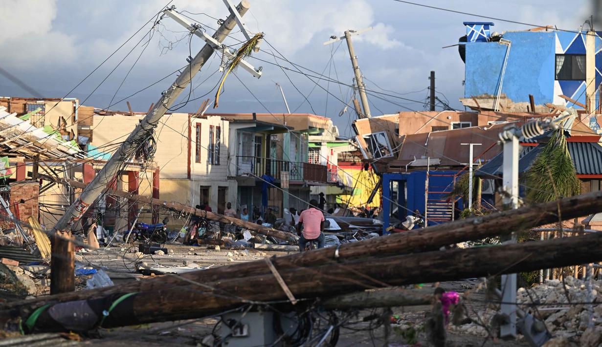 Tiang-tiang listrik tumbang saat seorang pria bersepeda melintasi lingkungan North Street yang hancur akibat Badai Melissa di Black River, Jamaika, pada 29 Oktober 2025. Empat rumah sakit mengalami kerusakan, dan satu di antaranya kehilangan pasokan listrik sehingga memaksa evakuasi 75 pasien. (Ricardo MAKYN/AFP)