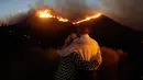 Roger Bloxberg dan istrinya, Anne berpelukan saat menyaksikan kebakaran di puncak bukit dekat rumah mereka di West Hills, California, AS, Jumat (9/11). Api Woolsey melahap ribuan hektare hutan dan menghancurkan banyak rumah. (AP Photo/Marcio Jose Sanchez)