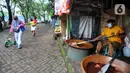 Warga bejalan kaki melewati pembuat dodol Betawi di Setu Babakan, Jagakarsa, Jakarta Selatan, Minggu (4/4/2021). Setu Babakan kembali dibuka untuk umum pada 27 Maret 2021 dengan menerapkan protokol kesehatan. (merdeka.com/Arie Basuki)
