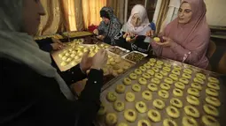 Perempuan Palestina membuat kue tradisional berisi kurma dan kacang-kacangan dalam persiapan untuk liburan Idul Fitri, di kota Hebron, Tepi Barat, pada 28 April 2022. Seluruh umat Muslim di dunia akan menandai berakhirnya bulan suci Ramadhan dengan Idul Fitri. (HAZEM BADER / AFP)