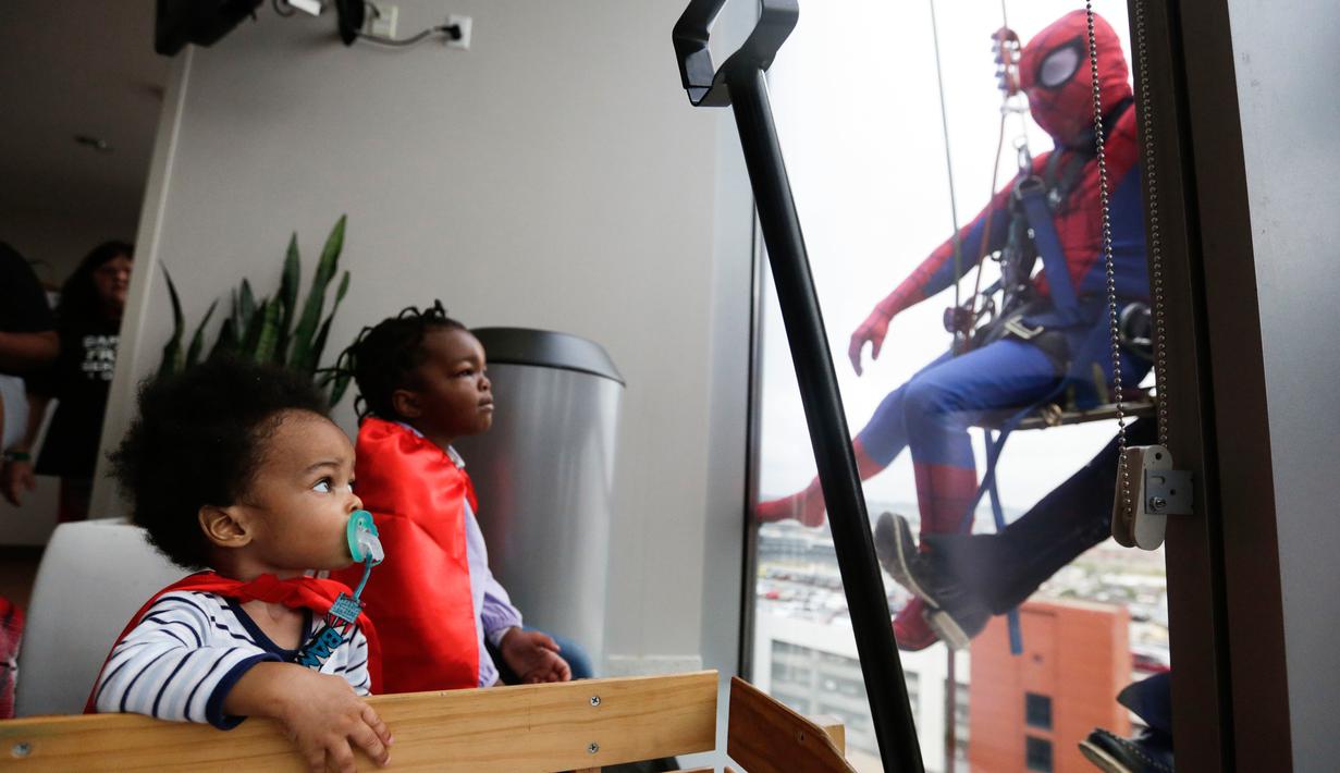Pasien anak mengamati superhero Spiderman membersihkan kaca jendela kamar sebuah rumah sakit di Birmingham, Rabu (11/10). Sekelompok superhero bekerja membersihkan jendela rumah sakit untuk menghibur anak- anak yang sedang sakit. (AP Photo/Brynn Anderson)