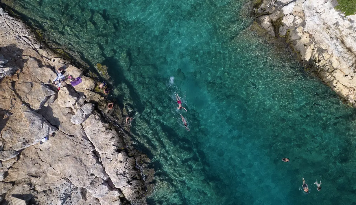Orang-orang berenang di laut di pinggiran Vouliagmeni, barat daya Athena, Yunani, Kamis (29/7/2021). Suhu naik di atas 40 C (104 F) di beberapa bagian Yunani dan sebagian besar wilayah Eropa. (AP Photo/Yorgos Karahalis)