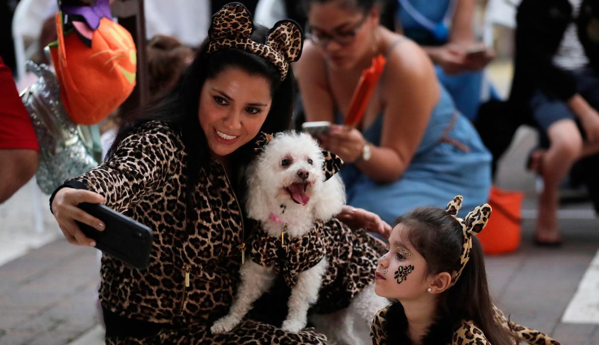 Diana Vargas (kiri) mengambil foto putrinya Naomi dengan anjing mereka Minnie saat mengikuti kontes kostum anjing Halloween tahunan di Coral Gables Museum, Coral Gables, Florida, Amerika Serikat, Kamis (31/10/2019). (AP Photo/Lynne Sladky)