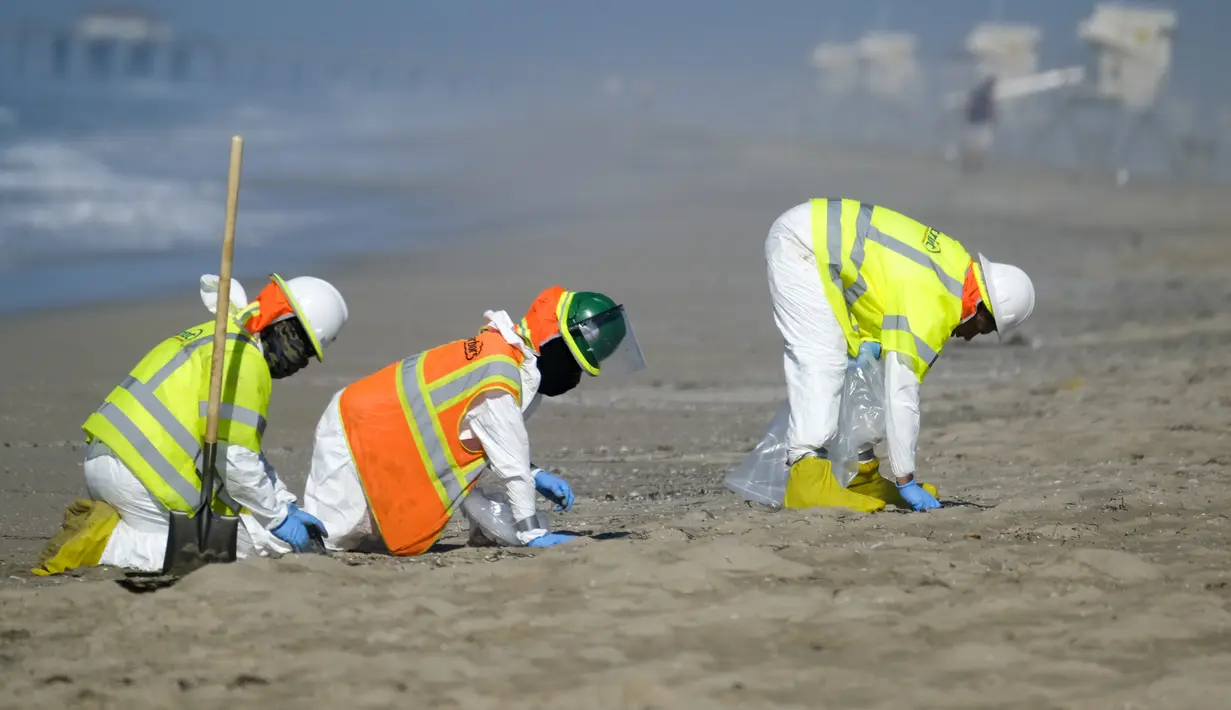 Pekerja dengan pakaian pelindung membersihkan pantai yang terkontaminasi tumpahan minyak di Huntington Beach, California, Amerika Serikat, Selasa (5/10/2021). Kebocoran pipa menyebabkan tumpahan minyak di lepas pantai California. (AP Photo/Ringo H.W. Chiu)