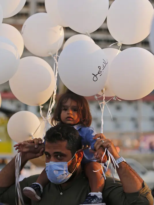 Pria dan anaknya memegang balon saat upacara untuk memperingati peristiwa ledakan pelabuhan 4 Agustus di Beirut, Lebanon, 4 Oktober 2020. Dua ledakan yang mengguncang Pelabuhan Beirut menghancurkan sebagian kota dan menewaskan sekitar 190 orang serta melukai 6.000 lainnya. (Xinhua/Bilal Jawich)