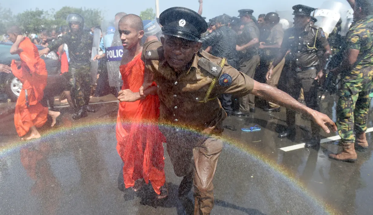 Seorang polisi mengamankan biksu saat aksi protes di kota pelabuhan selatan Hambantota, Sri Lanka (7/1). Mereka memprotes pembuatan zona industri untuk investasi China di sebuah kawasan di Sri Lanka. (AFP/ Ishara S. Kodikara)