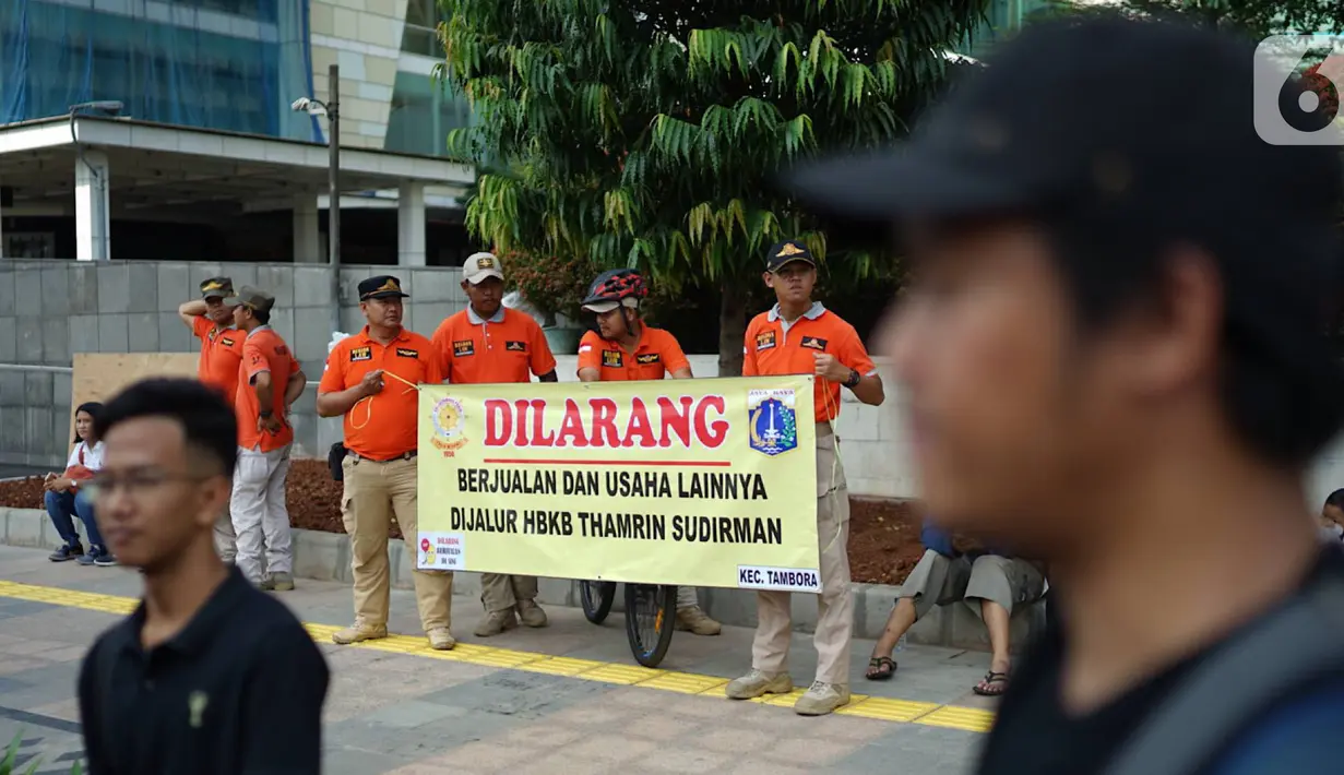 Petugas Satpol PP membentangkan spanduk larangan berjualan di jalur Hari Bebas Kendaraan Bermotor atau Car Free Day, Jakarta, Minggu (3/11/2019). Pemprov DKI melarang PKL berjualan di sepanjang jalur Car Free Day yang selama ini memenuhi badan jalan maupun trotoar. (Liputan6.com/Immanuel Antonius)