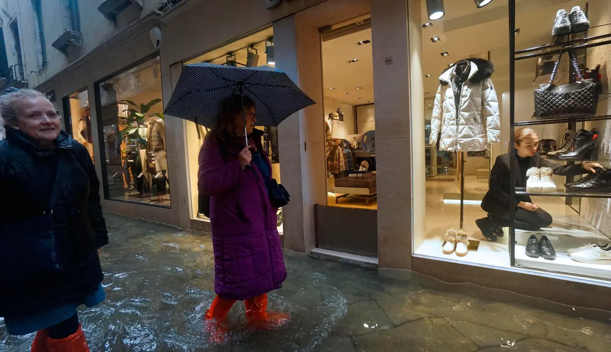 Pegawai toko merapikan sepatu saat warga berjalan di jalanan yang banjir akibat gelombang pasang yang menerjang Venesia, Italia, Selasa (12/11/2019). Venesia dilanda banjir akibat gelombang pasang setinggi 127 cm. (AP Photo/Luca Bruno)