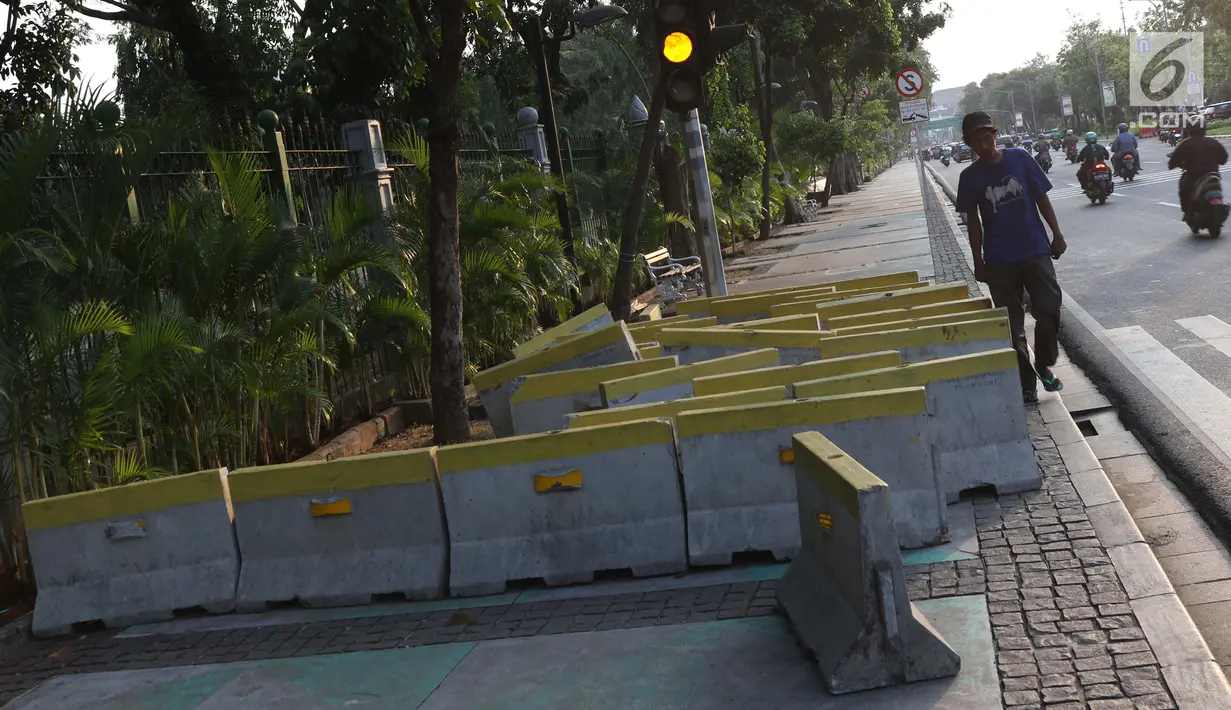 Pejalan kaki menghindari beton pembatas jalan yang diletakkan di atas trotoar Jalan Medan Merdeka Utara, Jakarta, Kamis (25/7/2019). Pembatas jalan yang berada tidak pada tempatnya mengganggu kenyamanan pejalan kaki yang melintasi trotoar jalan tersebut. (Liputan6.com/Helmi Fithriansyah)