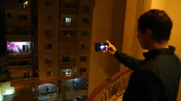 Warga mengabadikan foto konser biola yang digelar dari atas balkon di Kairo, pada 31 Maret 2020. Setiap malam, pemain biola asal Mesir Mohammed Adel menampilkan konser dari balkonnya untuk menghibur para tetangga selama jam malam nasional yang diberlakukan akibat COVID-19. (Xinhua/Ahmed Gomaa)