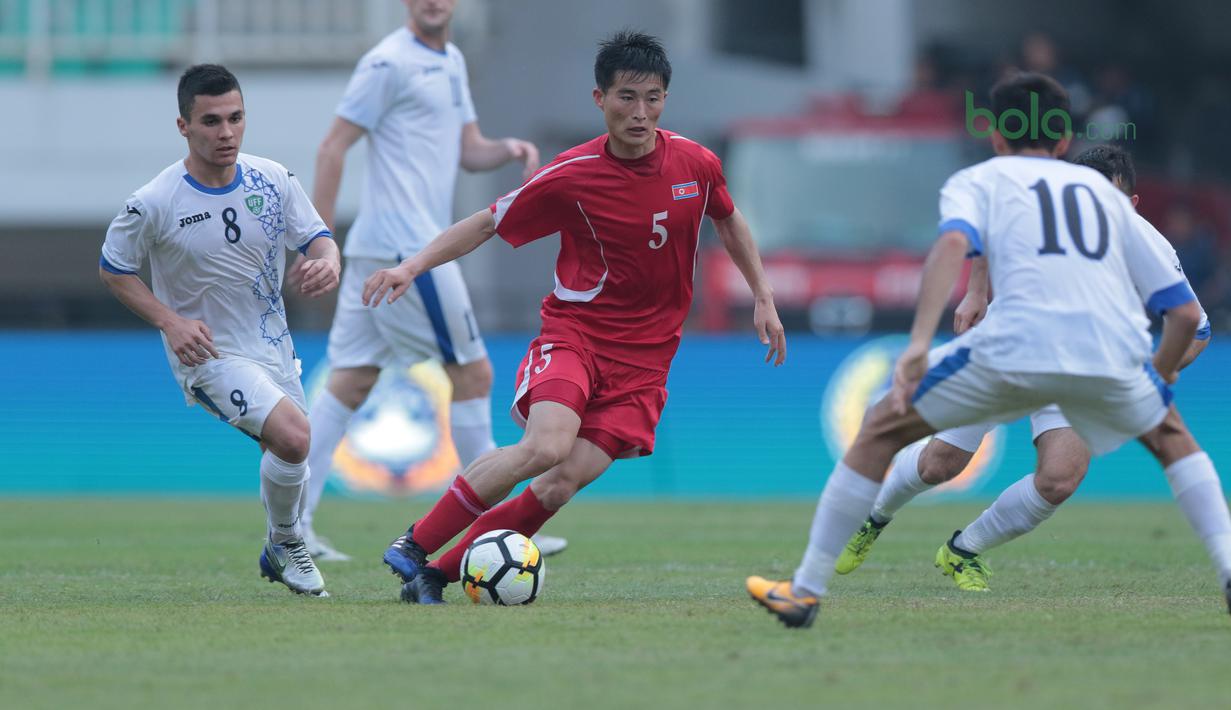 Pemain Korea Utara, Jon Se Gye berusaha melewati adangan pemain Uzbekistan pada laga PSSI Anniversary Cu 2018 di Stadion Pakansari, Bogor, (26/4/2018). Uzbekistan bermain imbang 2-2. (Bola.com/Nick Hanoatubun)