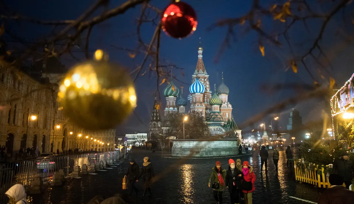 Wisatawan berjalan di kawasan Lapangan Merah atau Red Square dengan latar belakang Katedral St. Basil di Moskow, Rusia, Senin (18/12). Kawasan Red Square didekorasi dengan lampu dan pernak-pernik perayaan Natal dan Tahun Baru. (AP Photo/Pavel Golovkin)