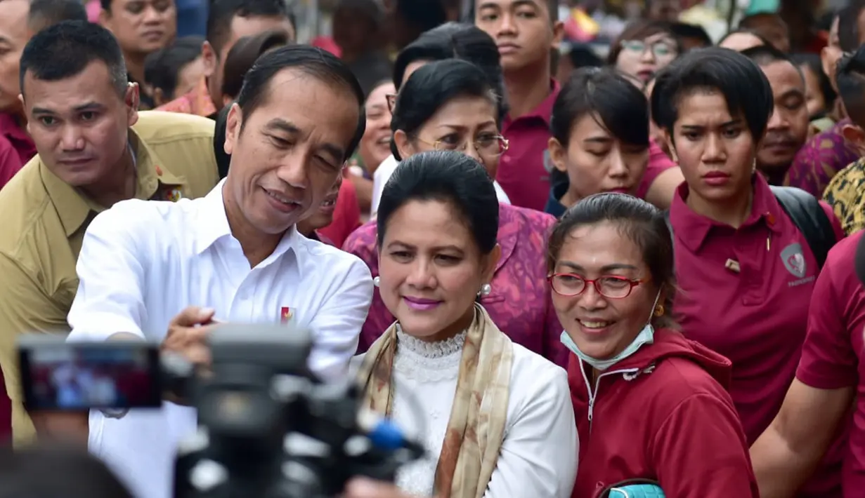 Presiden Joko Widodo ditemani Ibu Negara Iriana berswafoto dengan warga saat meninjau rencana revitalisasi Pasar Sukawati di Gianyar, Bali, Jumat (14/6/2019). Jokowi melihat rencana proyek revitalisasi Pasar Sukawati sekaligus berinteraksi dengan pedagang. (Liputan6.com/Pool/Biro Pers Setpres)