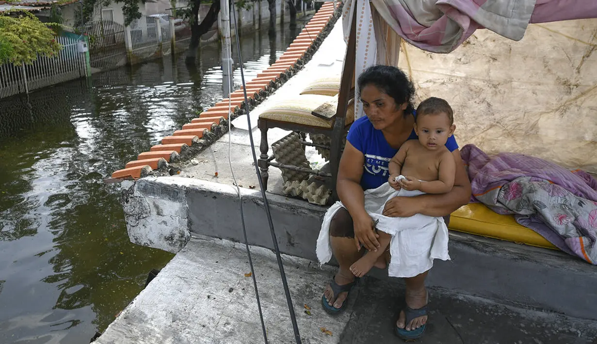 Seorang wanita dan anaknya duduk di atap rumah mereka yang terendam banjir di Mata Redonda, Maracay, Venezuela, Rabu (21/10/2020). Lusinan keluarga mencari perlindungan di atap rumah mereka untuk melindungi barang pribadi mereka. (AP Photo/Matias Delacroix)