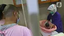 Perawat saat mempraktekan cara memandikan bayi kepada seorang ibu di RSIA Tambak, Jakarta, Kamis (18/02/2021). Melatih para ibu baru untuk memandikan bayi pertama tersebut dilakukan dengan menerapkan protokol kesehatan ketat. (Liputan6.com/Herman Zakharia)