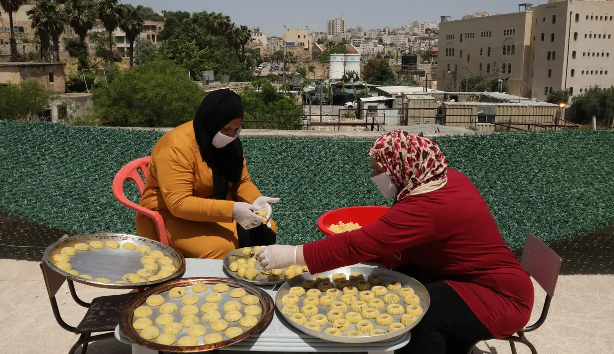 Perempuan Palestina dengan masker dan sarung tangan menyiapkan biskuit tradisional menjelang Idul Fitri di atap rumah mereka di kota tua Hebron, Tepi Barat yang diduduki, Selasa (19/5/2020). Biskuit-biskuit itu akan dijual secara online guna menjaga jarak selama pandemi Covid-19. (HAZEM BADER/AFP)