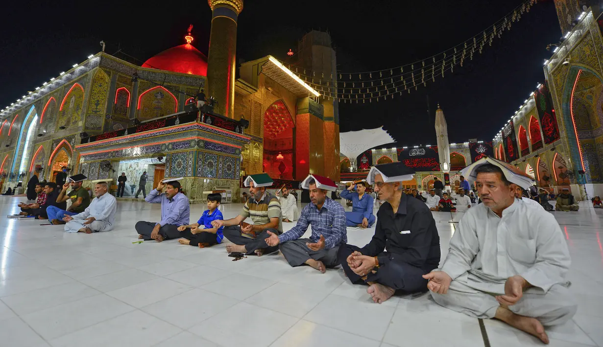Para jemaah syiah manaruh kitab suci Al-Quran di atas kepala mereka saat menyambut malam lailatul qadar di Makam Suci Imam Ali, Najaf, Irak, Sabtu (16/5/2020). Ritual saat berdoa dan meminta hajat kepada Tuhan ini sudah berlangsung selama berabad-abad lamanya. (HAIDAR HAMDANI/AFP)