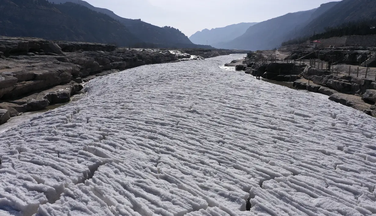 Pemandangan dari udara terlihat Sungai Kuning yang tertutup es di dekat tempat wisata Air Terjun Hukou di Provinsi Shaanxi, China pada 16 Desember 2020. Air terjun Hukou menyuguhkan pemandangan musim dingin nan spektakuler saat suhu udara terus turun dalam beberapa hari terakhir. (Xinhua/Tao Ming)