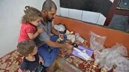 Warga Suriah, Hadheefa al-Shahadh ditemani anak-anaknya saat membuat masker gas untuk menghadapi serangan pasukan pemerintah di Desa Maud Shurin, Provinsi Idlib, Selasa (11/). Cara membuat masker gas dia pelajari dari Youtube. (OMAR HAJ KADOUR/AFP)