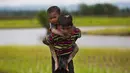 Seorang pemuda etnis Rohingya dari Myanmar menggendong anak kecil di punggungnya saat berjalan melewati sawah untuk menyebrang ke perbatasan Bangladesh, wilayah Teknaf yang berada di distrik Cox's Bazar, 1 September 2017. (AP Photo/Bernat Armangue)