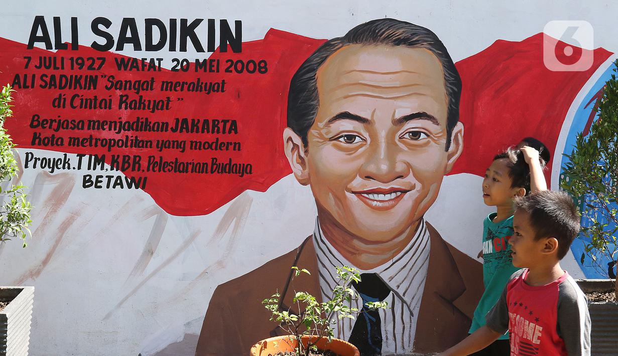 Anak-anak melintasi mural di Kampung Budaya Kawasan Jakarta Barat, Selasa (19/11/2019). Penataan dilakukan mulai daari pembenahan jalan, pembuatan resapan air, bangku, mural, hingga ubin pemandu untuk penyandang disabilitas dengan anggaran mencapai Rp2.5 miliar. (Liputan6.com/Herman Zakharia)