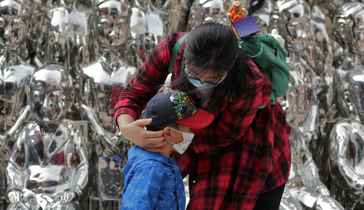 Seorang wanita membantu seorang anak mengenakan masker untuk mengekang penyebaran COVID-19 di Beijing, China, Minggu (11/10/2020). Meski penyebaran COVID-19 hampir diberantas di China, pandemi masih melonjak di seluruh dunia dengan jumlah kematian yang terus meningkat. (AP Photo/Andy Wong)