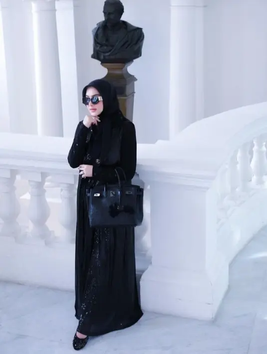 Syahrini tampil serba hitam dengan dress shimmer dan kerudungnya, lengkap mengenakan flat shoes. Ia menutupi perutnya dengan tas Hermes hitam seharga Rp2.750.000.000. [@princessyahrini]
