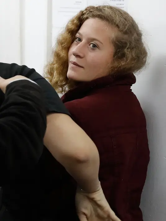 Ekspresi Ahed Tamimi saat ditahan di pengadilan militer, penjara Ofer milik Israel di Desa Betunia (20/12). Ahed Tamimi ternyata tak sendirian, tentara Israel juga menangkap sang ayah, Basem al Tamimi dan sepupunya, Nur. (AFP Photo/Ahmad Gharabli)