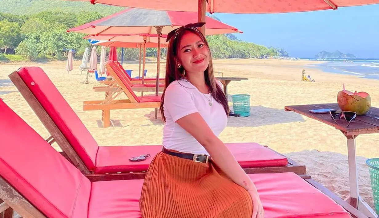 Vita Alvia sering kali mengunggah momen liburan di akun Instagram pribadinya. Penyanyi yang berasal dari Banyuwangi tersebut kerap berlibur ke pantai. Penampilannya dengan baju putih dan rok panjang berwarna oranye, ia tampak bahagia bersantai di kursi pantai. (liputan6.com/IG/@iam_vitaalvia)