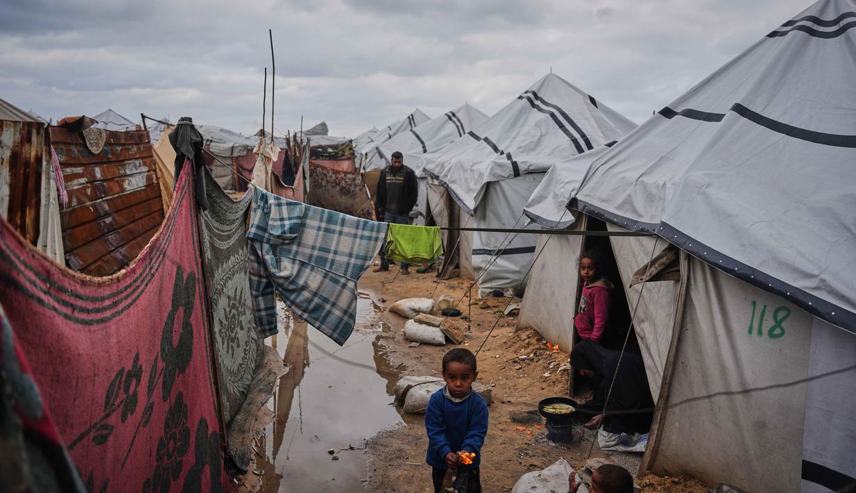 Hujan deras menyebabkan banjir di sejumlah kamp-kamp pengungsian, termasuk wilayah Nuseirat, Al-Mawasi dan Khan Younis. Tampak dalam foto, Nanaa Abu Jari memasak di luar tendanya setelah tenda tersebut terendam air hujan di Nuseirat, Jalur Gaza tengah, Jumat, 2 Januari 2026. (AP Photo/Abdel Kareem Hana)