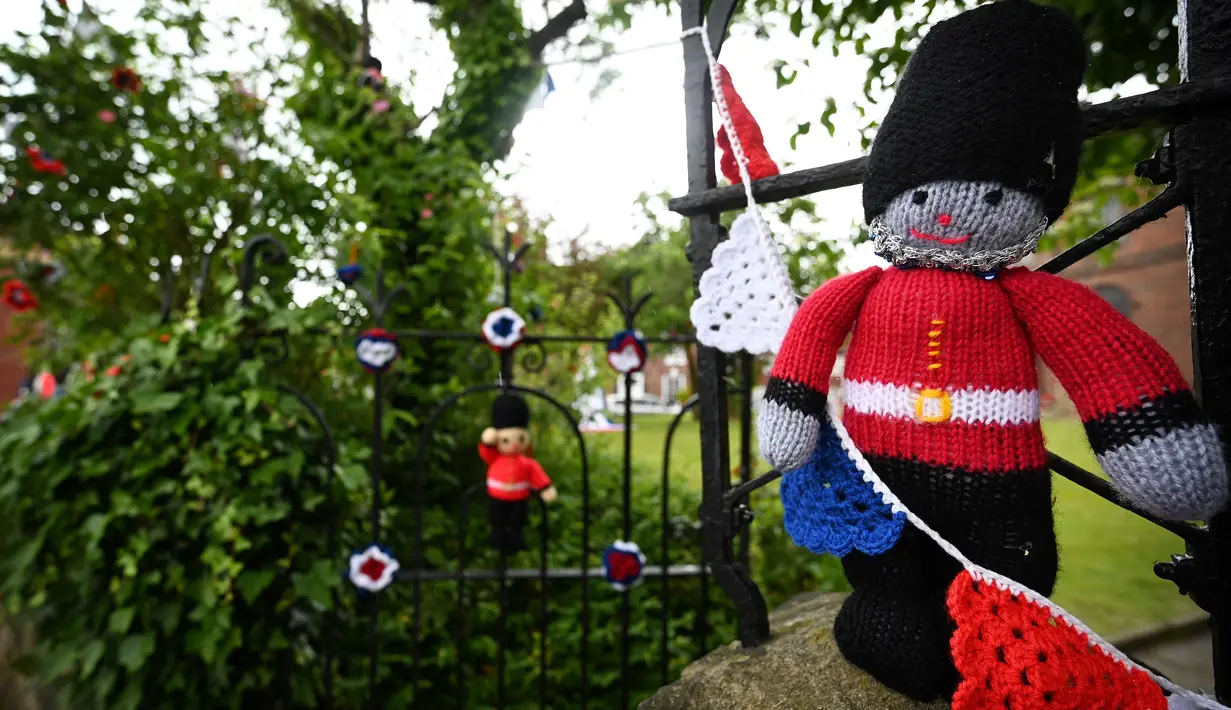 Boneka penjaga Inggris rajutan terpasang di gerbang Gereja St Luke di Kapel Holmes, barat laut Inggris, pada 30 Mei 2022. Sebuah kelompok masyarakat lokal, The Holmes Chapel Community Yarn Bombers telah memenuhi desa dengan barang-barang rajutan patriotik untuk merayakan Platinum Jubilee Ratu. (Paulus ELLIS / AFP)