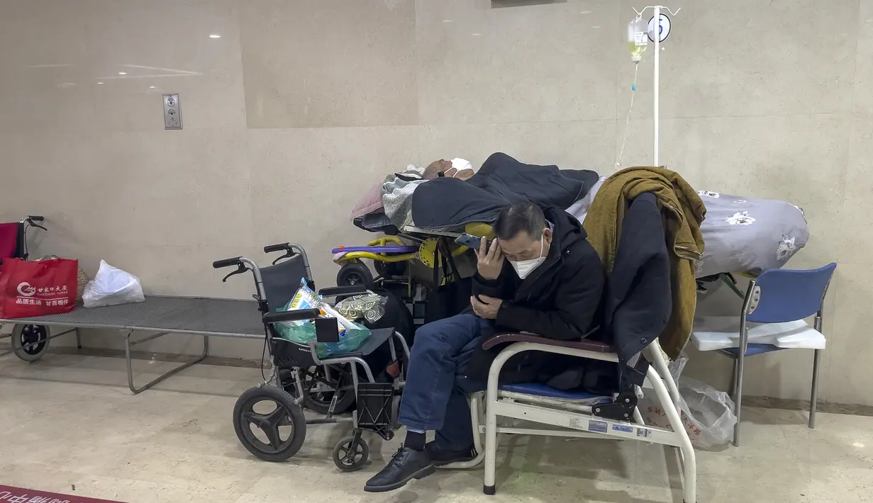 Seorang pria mendengarkan teleponnya ketika dia merawat kerabatnya yang lanjut usia di koridor bangsal darurat untuk menerima infus di sebuah rumah sakit di Beijing, Kamis (5/1/2023). Pasien, kebanyakan dari mereka lansia, berbaring di tandu di lorong dan menerima oksigen sambil duduk di kursi roda saat kasus COVID-19 melonjak di ibu kota China, Beijing. (AP Photo/Andy Wong)
