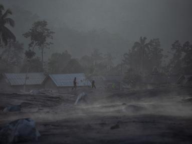 Orang-orang berjalan melewati rumah-rumah menyusul letusan gunung berapi oleh Gunung Semeru di desa Kajar Kuning di Lumajang (5/12/2022). Gunung Semeru meletus pada tanggal 4 Desember memuntahkan awan abu panas setinggi satu mil dan sungai lava di sisinya sambil memicu evakuasi hampir 2.000 orang tepat satu tahun setelah letusan besar terakhirnya menewaskan puluhan orang. (AFP/Juni Kriswanto)