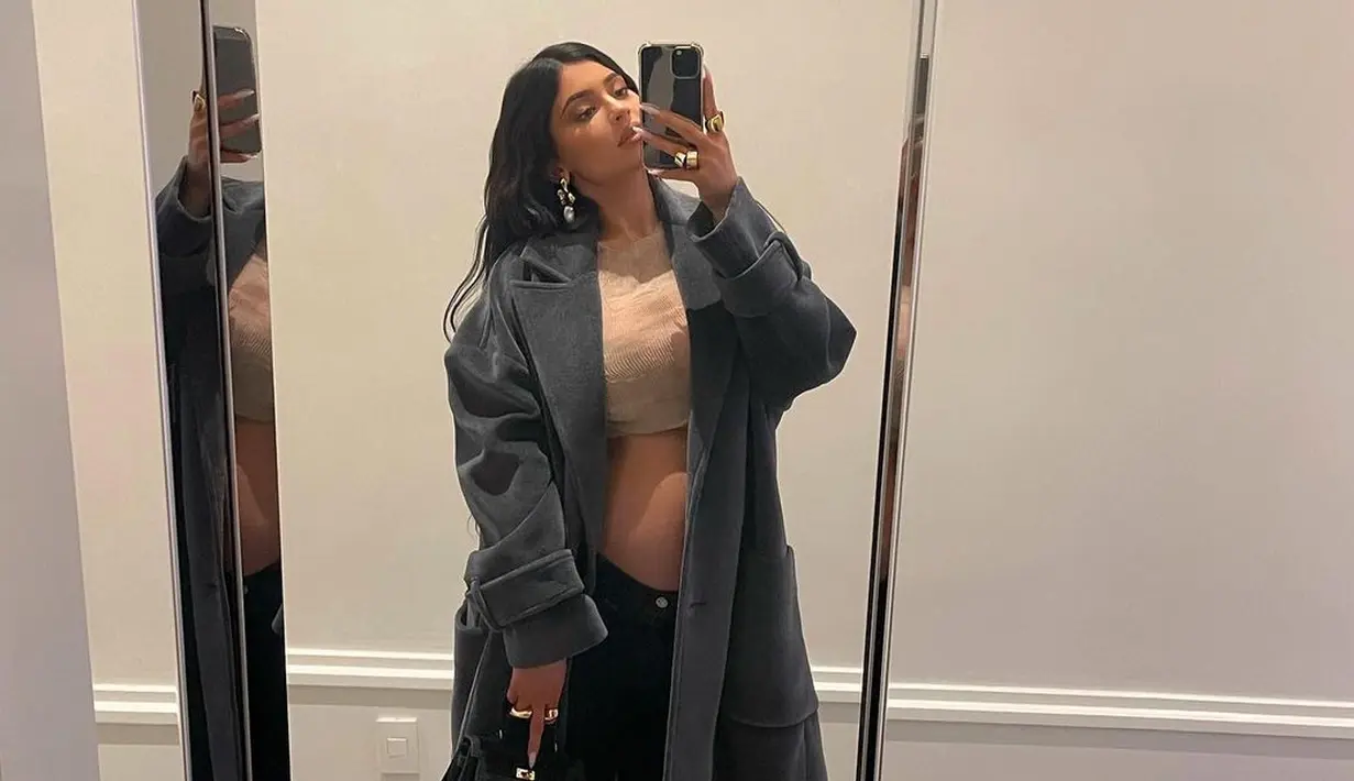 Kembali berfoto selfie, Kylie Jenner memperlihatkan baby bump yang baru mulai muncul. Dengan crop top cokelat yang ditumpuknya dengan long coat abu-abu, ia padu dengan jogger pants, sepatu, dan mini bag hitam. Foto: Instagram.