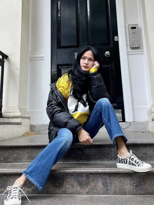 Berpose sambil duduk, Donna mengenakan outfit seperti jaket padding hitam dengan inner kuning yang cukup simpel dengan bawahan denim dan sneaker Diornya. (@donnaharunofficial)