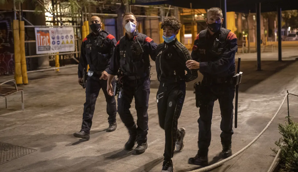 Seorang pemuda ditahan oleh Mossos d'Escuadra, kepolisian regional Catalonia, setelah jam malam di Barcelona pada 1 November 2020. Pemerintah Spanyol menetapkan pembatasan gerak atau jam malam yang berlaku pukul 22.00 untuk mengendalikan lonjakan kasus Covid-19. (AP Photo/Emilio Morenatti)