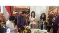 Ahok yang mengenakan kemeja batik ungu sedang memotong nasi tumpeng, yang akan diberikan kepada sang istri.