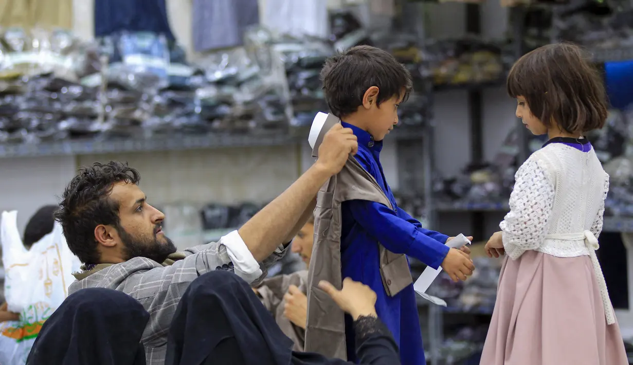 Warga Yaman membantu memilihkan pakaian baru untuk anak-anak mereka di ruang pamer yang membagikan pakaian kepada para pemuda yang kehilangan orang tua dalam konflik, sebagai bagian dari kegiatan amal selama bulan suci Ramadhan, di ibu kota Sanaa (8/4/2022). (AFP/Mohammed Huwais)