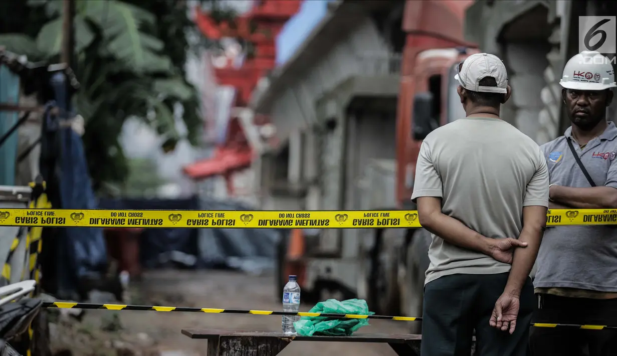 Pekerja berjaga di dekat garis polisi usai ambruknya crane pengerjaan proyek double-double track kereta api di Jatinegara, Jakarta, Minggu (4/2). (Liputan6.com/Faizal Fanani)