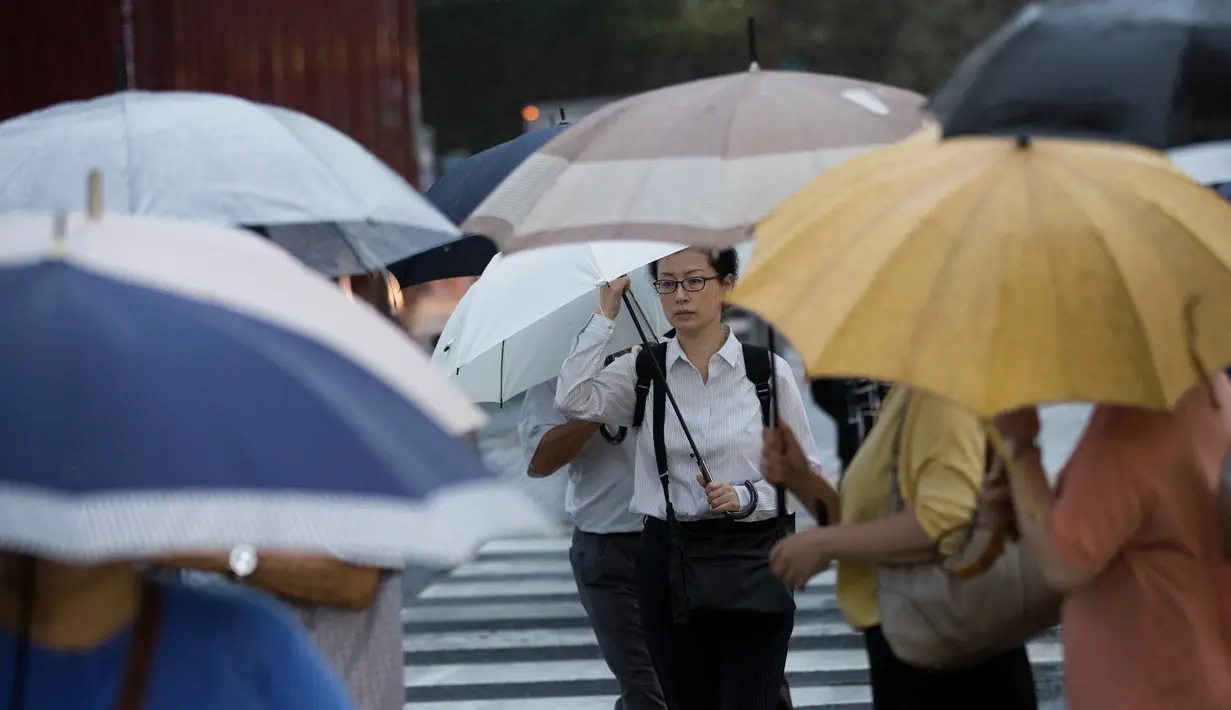 Pejalan kaki menggunakan payung berjalan saat hujan turun di Tokyo, Jepang (8/8). Topan kuat sedang mengarah ke Jepang pada 8 Agustus, mendorong badan cuaca untuk memperingatkan akan terjadi hujan lebat dan angin kencang. (AFP Photo/Behrouz)