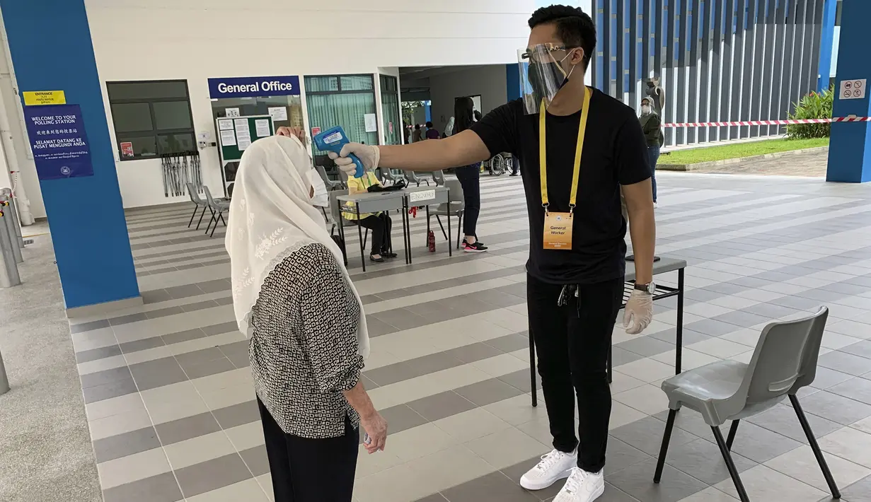 Petugas memeriksa suhu tubuh pemilih yang memberikan suara dalam pemilu di TPS Dunearn Secondary School, Singapura Jumat (10/7/2020). Pemilu di tengah pandemi COVID-19, warga Singapura memberikan suara mereka dengan mengenakan masker dan sarung tangan plastik. (AP Photo/Royston Chan)