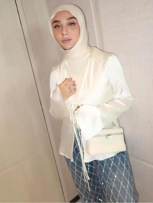 Margin tampil white on white dengan kerudung pashmina dipadukan inner dan outer satin lengan panjang bertali warna putih, senada dengan tasnya. Ia pun mengenakan bawahan rok denim bling-bling. [@marginw]