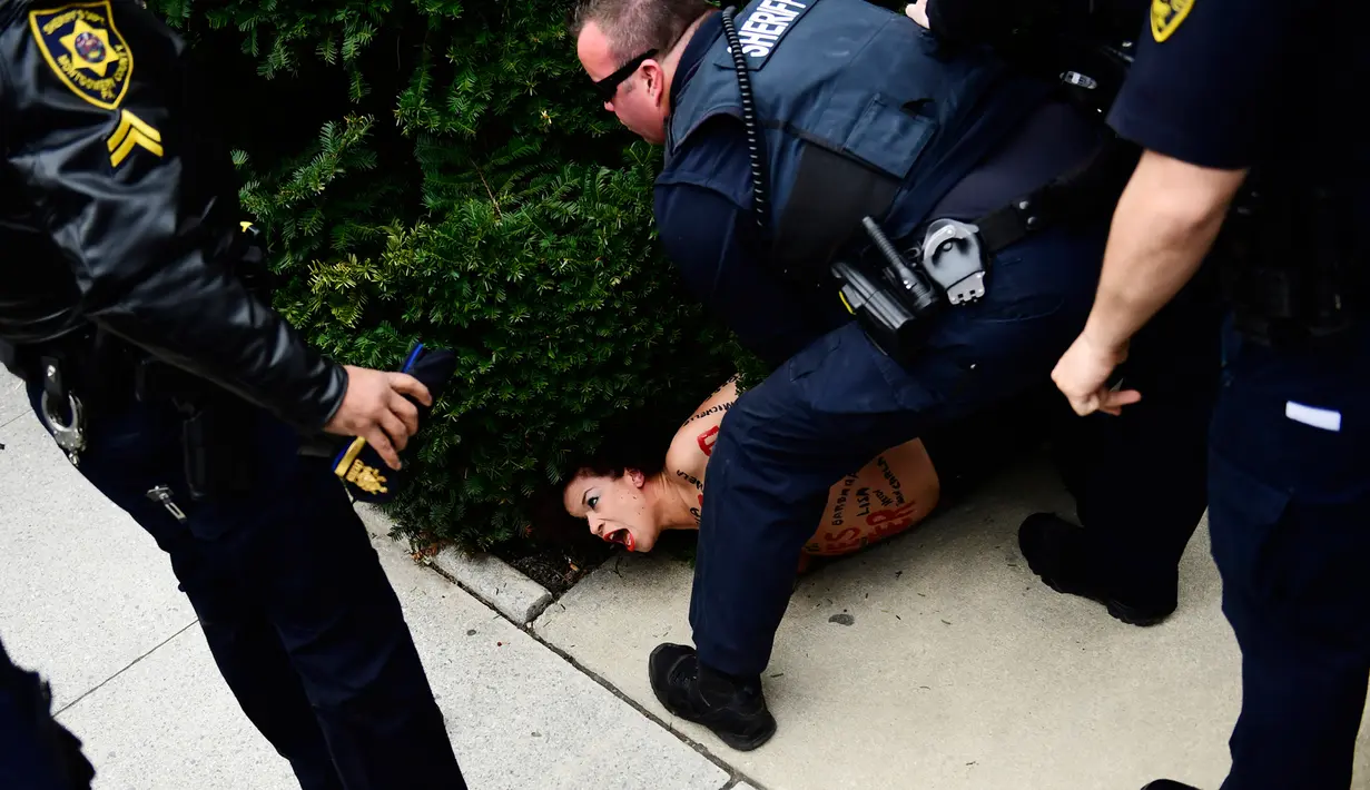 Polisi menahan pengunjuk rasa wanita yang tampil topless di sidang kekerasan seksual komedian Bill Cosby, Pennsylvania, AS, Senin (9/4). Cosby dikenal publik sebagai "America's Dad" pada dekade tahun 1980 dan 1990-an. (AP Photo/Corey Perrine)