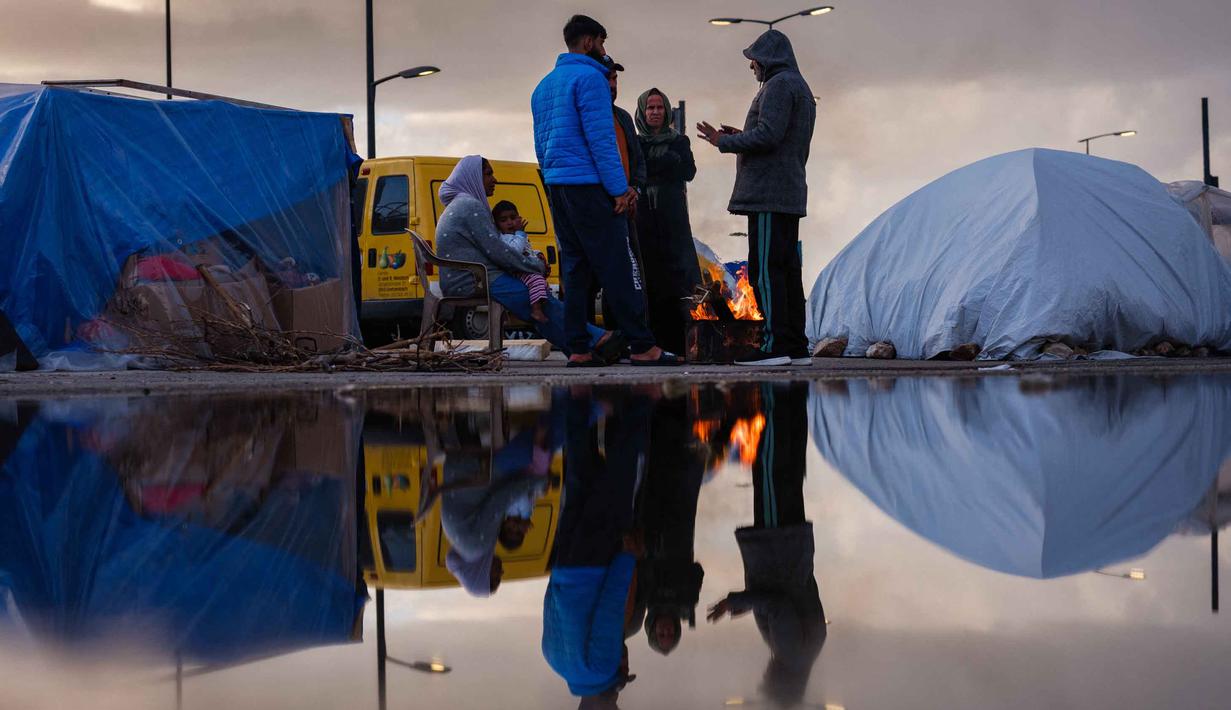 Israel mengklaim tindakan ini sebagai respons atas serangan dari kelompok Hizbullah. Tampak dalam foto, para pengungsi menghangatkan diri di sekitar api unggun di luar tenda mereka di sepanjang kawasan tepi laut Beirut, Lebanon, pada Senin 30 Maret 2026. (Dimitar DILKOFF/AFP)
