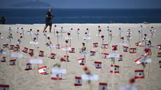 Seorang pria berjalan melewati 245 mawar yang ditempatkan oleh LSM Rio da Paz beserta nama korban dan bendera Lebanon untuk memperingati 3 tahun sejak ledakan Beirut 2020 di Pantai Copacabana, Rio de Janeiro, Brasil, diambil pada 4 Agustus 2023. (AFP/Carl De Souza)